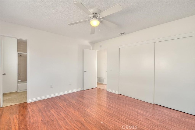 unfurnished bedroom with ensuite bathroom, a closet, a textured ceiling, and light wood-type flooring