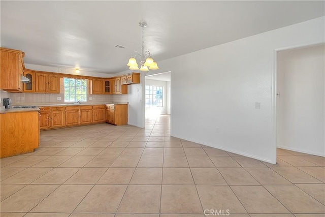 kitchen with light tile patterned flooring, tasteful backsplash, sink, hanging light fixtures, and a notable chandelier