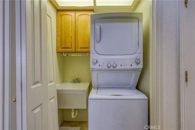 laundry room with cabinets, stacked washer / dryer, and sink