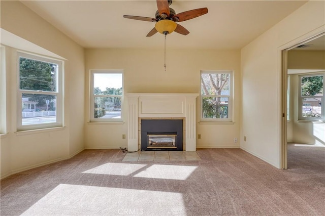 unfurnished living room featuring ceiling fan, a healthy amount of sunlight, a tile fireplace, and light carpet