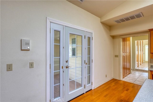 entryway with vaulted ceiling, light hardwood / wood-style floors, and french doors