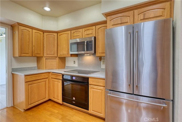 kitchen featuring light hardwood / wood-style flooring, decorative backsplash, light brown cabinetry, and black appliances