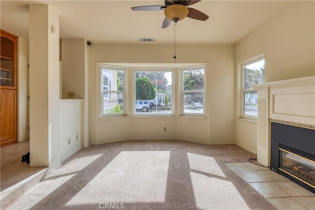 unfurnished living room with ceiling fan, a tiled fireplace, and light carpet