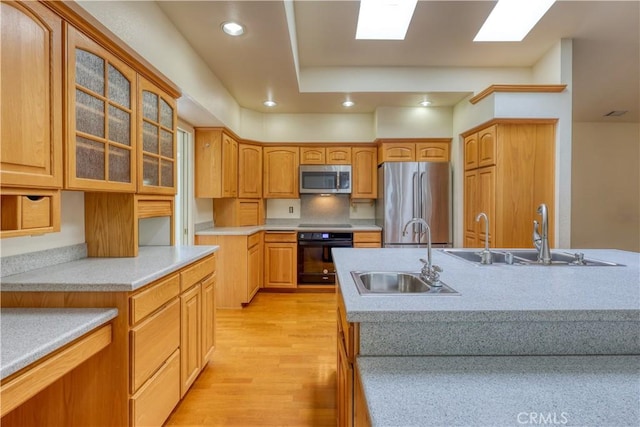 kitchen with a center island with sink, sink, light hardwood / wood-style flooring, and black appliances