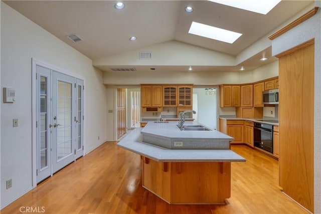 kitchen with sink, light hardwood / wood-style flooring, a breakfast bar area, black appliances, and an island with sink