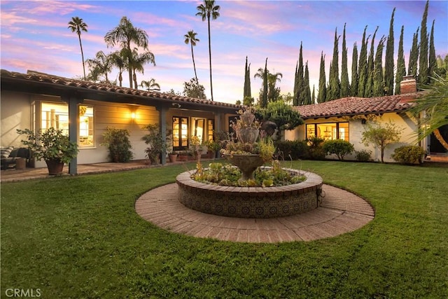 back house at dusk featuring a lawn