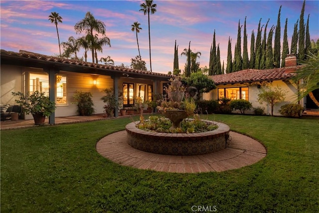 back of house featuring stucco siding, a lawn, and a tile roof