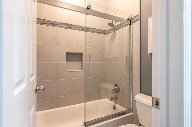 bathroom featuring toilet and shower / bath combination with glass door