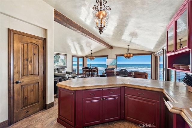 kitchen featuring an inviting chandelier, pendant lighting, lofted ceiling with beams, and a water view