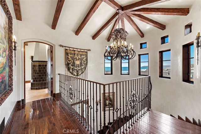 hallway featuring hardwood / wood-style flooring, a towering ceiling, a chandelier, and beamed ceiling