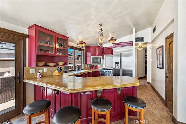 kitchen with a breakfast bar area, hanging light fixtures, built in appliances, tasteful backsplash, and kitchen peninsula