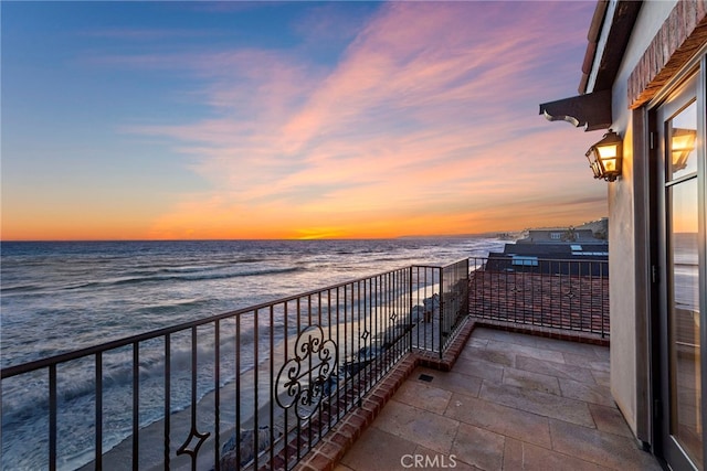 balcony at dusk featuring a water view