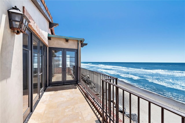 balcony featuring a view of the beach, a water view, and french doors