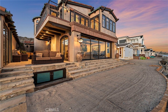 back house at dusk with a patio area, outdoor lounge area, and a balcony