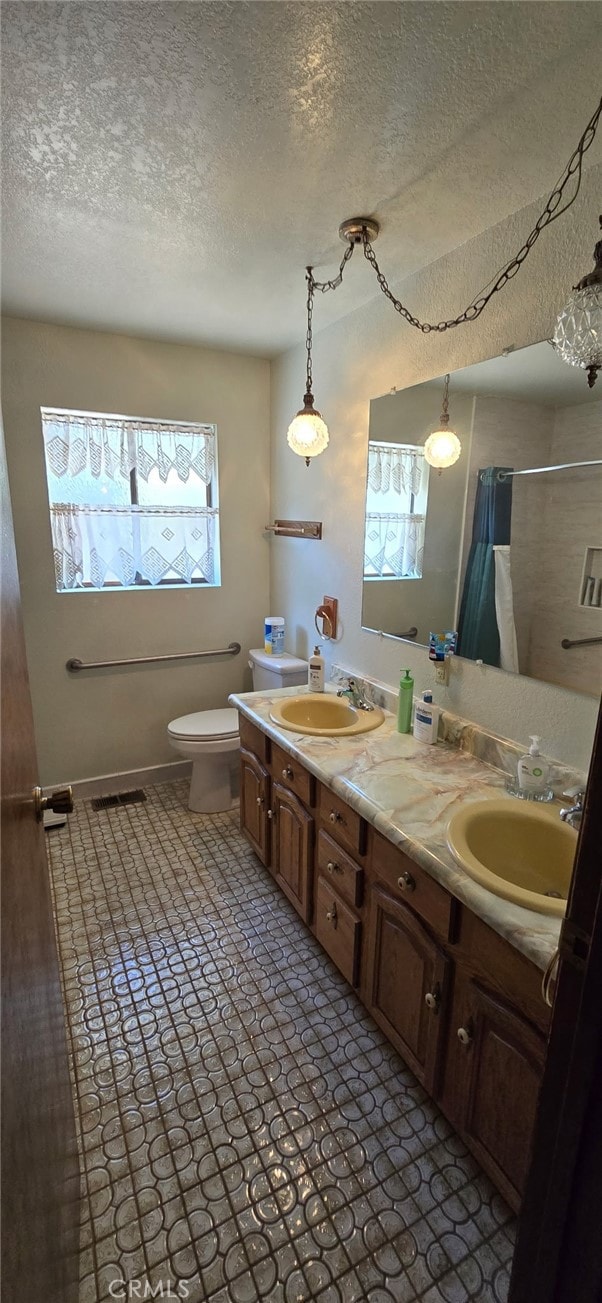 bathroom with double vanity, a textured ceiling, a sink, and toilet