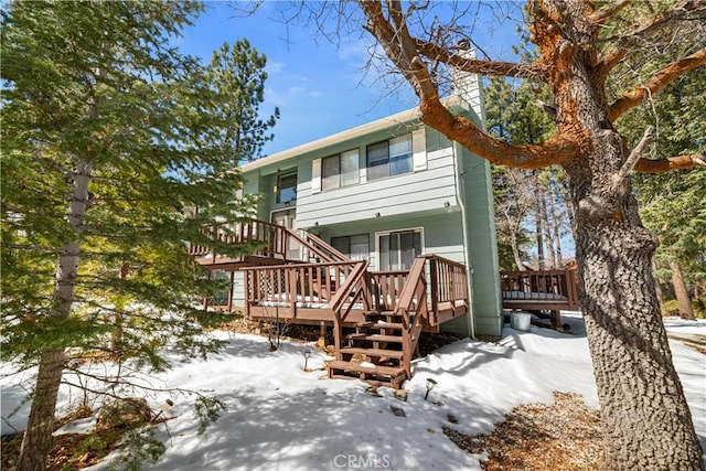 snow covered rear of property featuring a wooden deck and stairway
