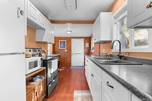 kitchen featuring sink, wood walls, hardwood / wood-style flooring, white appliances, and white cabinets