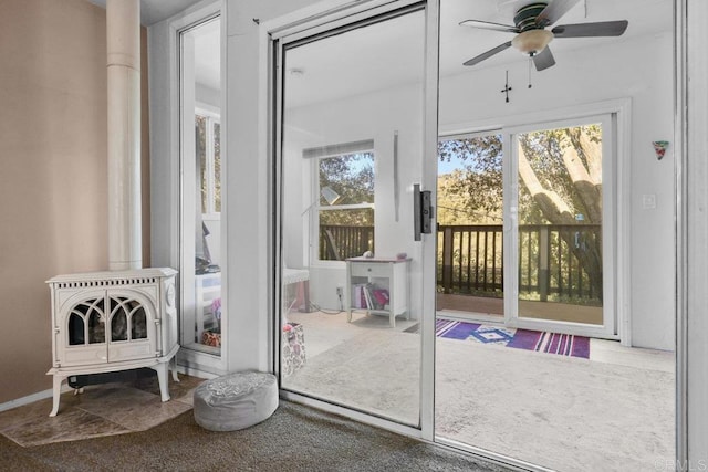 doorway to outside with ceiling fan, a healthy amount of sunlight, carpet floors, and a wood stove