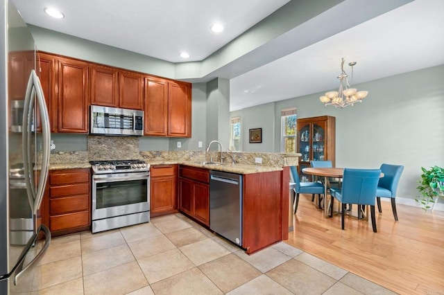 kitchen featuring pendant lighting, light stone countertops, kitchen peninsula, and appliances with stainless steel finishes