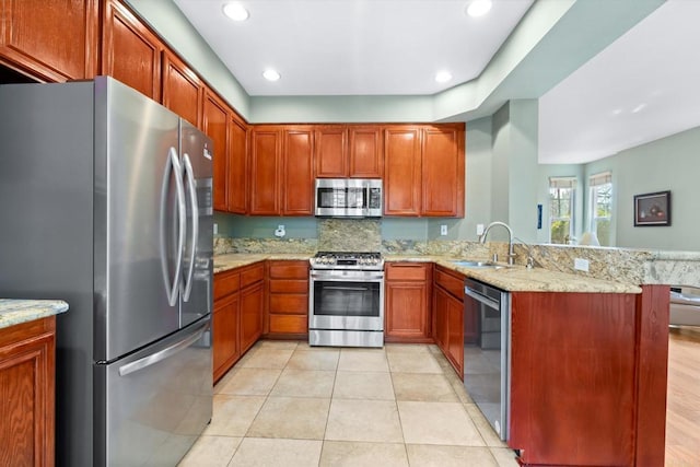 kitchen with light stone counters, stainless steel appliances, kitchen peninsula, and sink