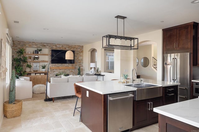 kitchen featuring appliances with stainless steel finishes, pendant lighting, sink, a kitchen island with sink, and dark brown cabinetry