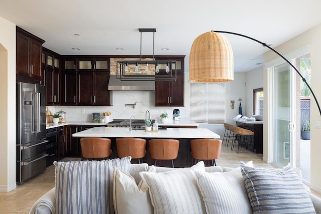 kitchen with a kitchen island with sink, dark brown cabinets, tasteful backsplash, and high quality fridge