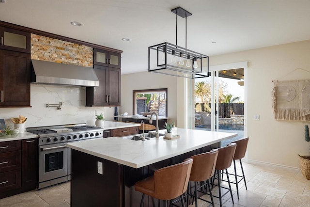 kitchen with sink, a center island with sink, double oven range, wall chimney range hood, and backsplash