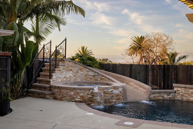 pool at dusk with an in ground hot tub and pool water feature