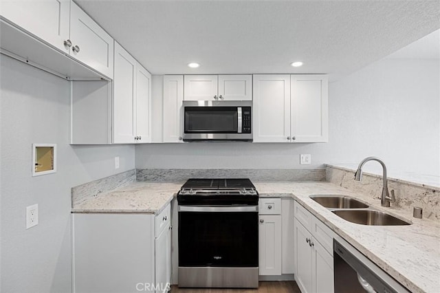 kitchen with appliances with stainless steel finishes, light stone countertops, sink, and white cabinets