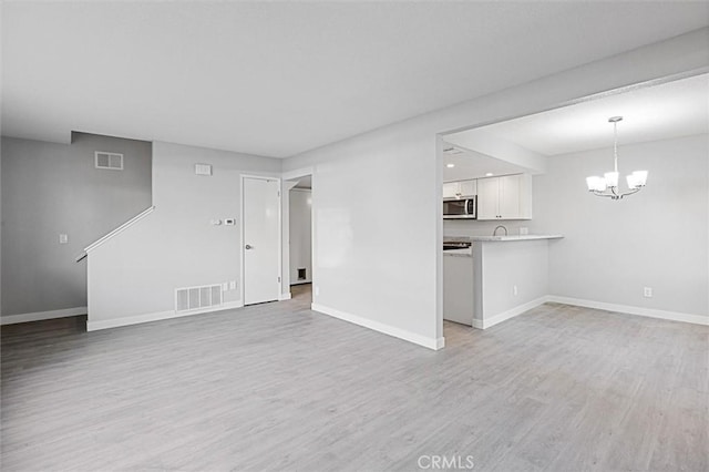 unfurnished living room featuring a chandelier and light hardwood / wood-style flooring