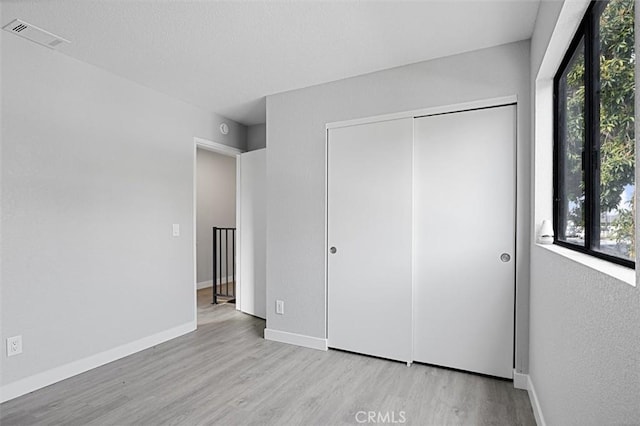 unfurnished bedroom with a closet, multiple windows, and light wood-type flooring