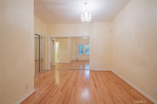 unfurnished room featuring a notable chandelier and light wood-type flooring