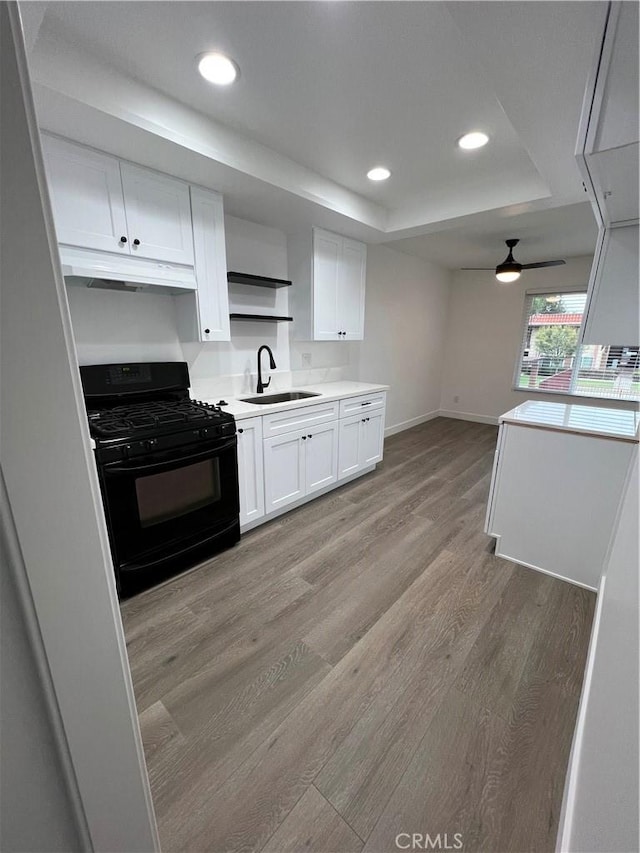 kitchen featuring black gas range oven, sink, light hardwood / wood-style flooring, white cabinets, and a raised ceiling