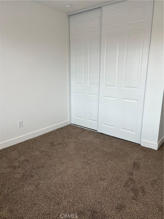 unfurnished bedroom with a closet and dark colored carpet