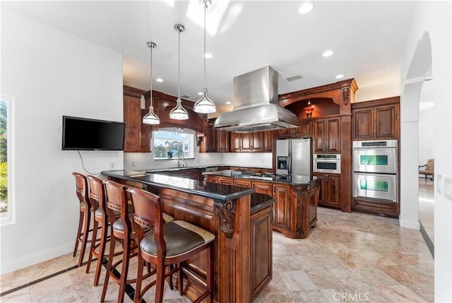 kitchen featuring appliances with stainless steel finishes, pendant lighting, island range hood, a kitchen bar, and kitchen peninsula