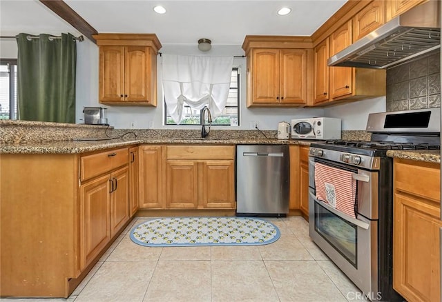 kitchen featuring appliances with stainless steel finishes, stone countertops, sink, light tile patterned floors, and wall chimney range hood