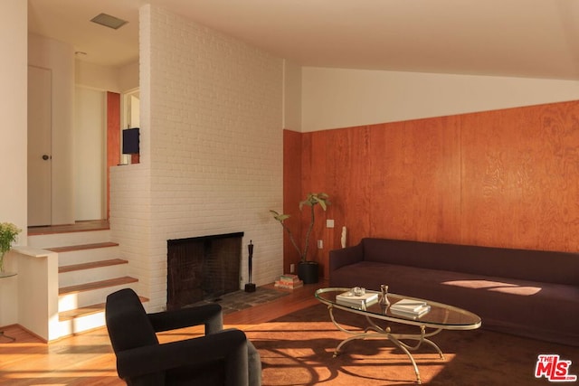 living room with a brick fireplace, wood-type flooring, and vaulted ceiling