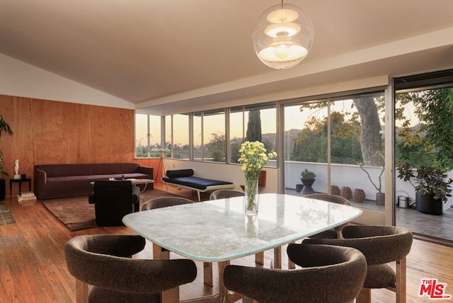 dining area with wood-type flooring, wooden walls, and vaulted ceiling