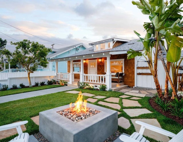 view of front facade featuring covered porch, a fire pit, and a front yard