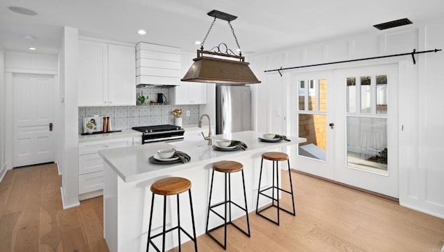 kitchen featuring stainless steel appliances, hanging light fixtures, a center island with sink, and white cabinets