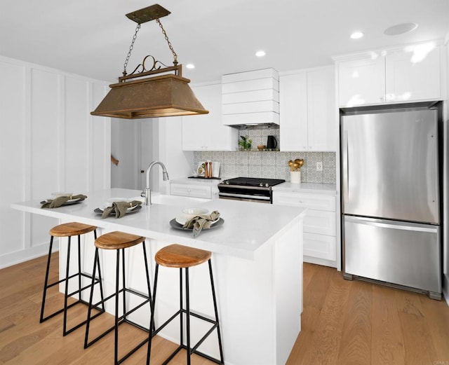 kitchen featuring an island with sink, white cabinetry, sink, stainless steel appliances, and light wood-type flooring