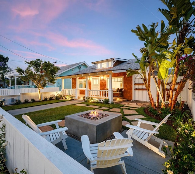 back house at dusk featuring a porch and an outdoor fire pit