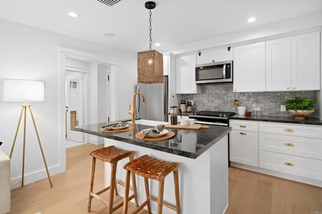 kitchen with white cabinetry, appliances with stainless steel finishes, an island with sink, and light hardwood / wood-style floors