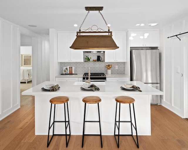 kitchen with white cabinetry, custom range hood, stainless steel refrigerator, and a center island with sink