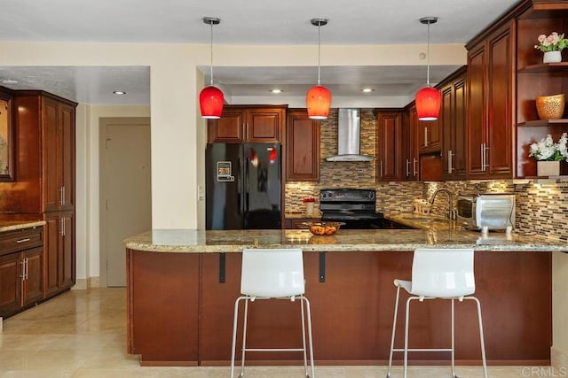 kitchen with wall chimney exhaust hood, a breakfast bar, black fridge, electric range, and kitchen peninsula