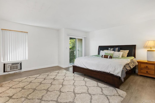 bedroom featuring a wall unit AC, access to exterior, baseboards, and wood finished floors