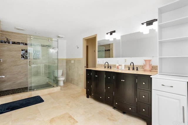 bathroom with double vanity, toilet, a sink, a shower stall, and tile walls