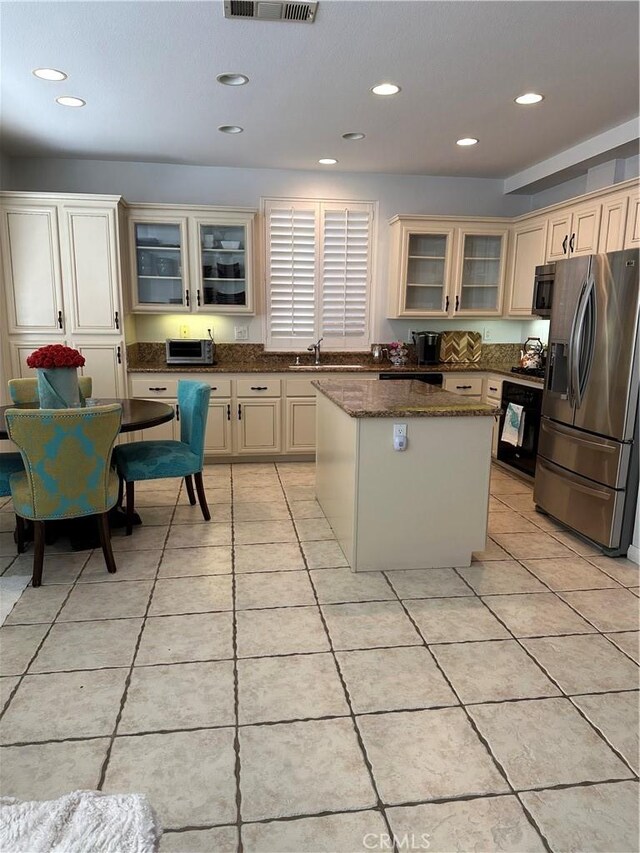 kitchen with a kitchen island, appliances with stainless steel finishes, light tile patterned floors, and cream cabinetry