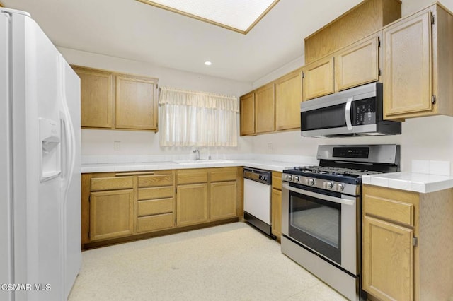 kitchen with appliances with stainless steel finishes, tile counters, light brown cabinetry, and sink