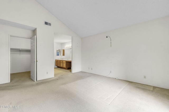 unfurnished bedroom featuring high vaulted ceiling, a walk in closet, light colored carpet, ensuite bath, and a closet